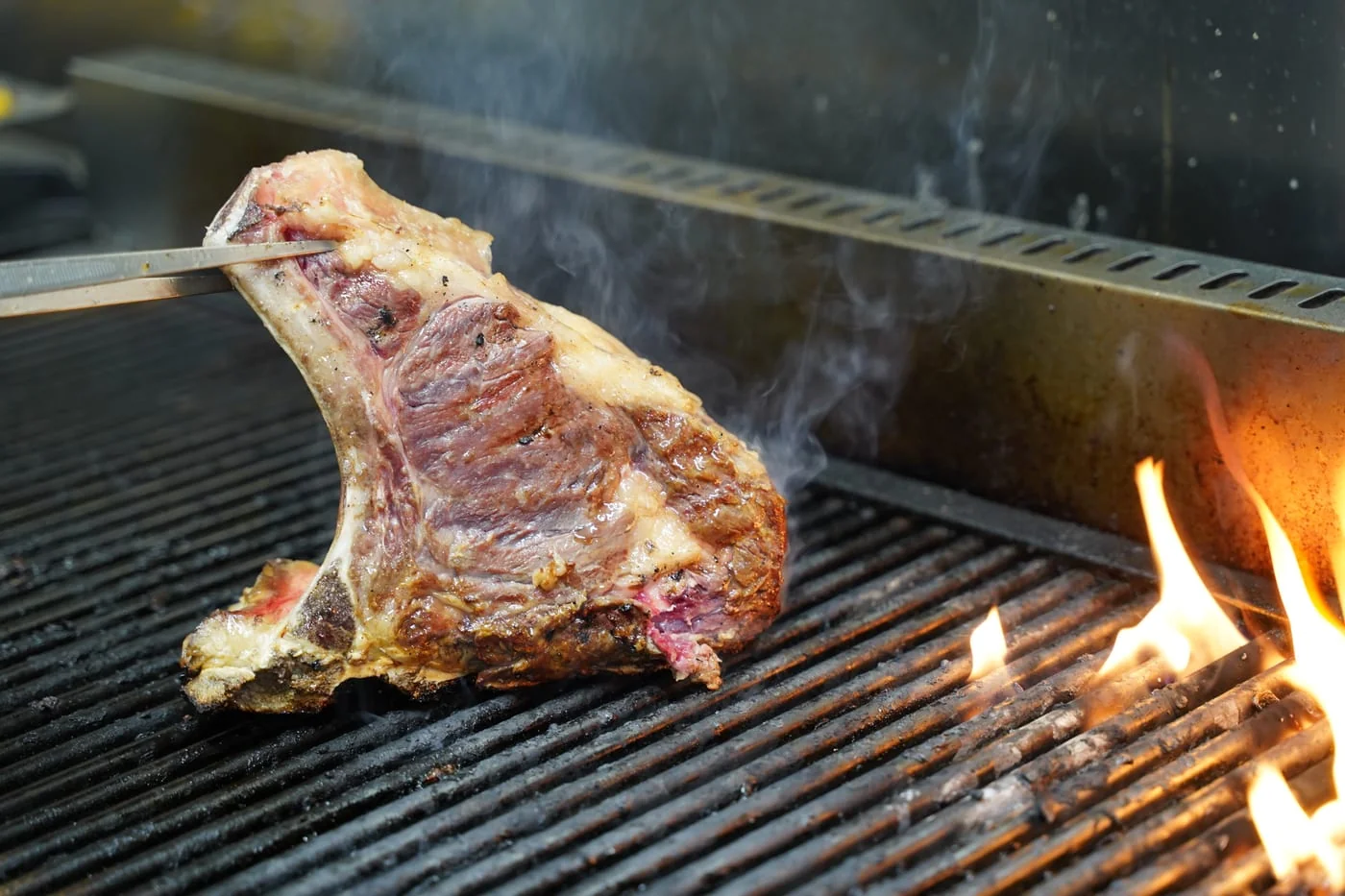Una bistecca alla fiorentina sulla griglia, con la fiamma accanto