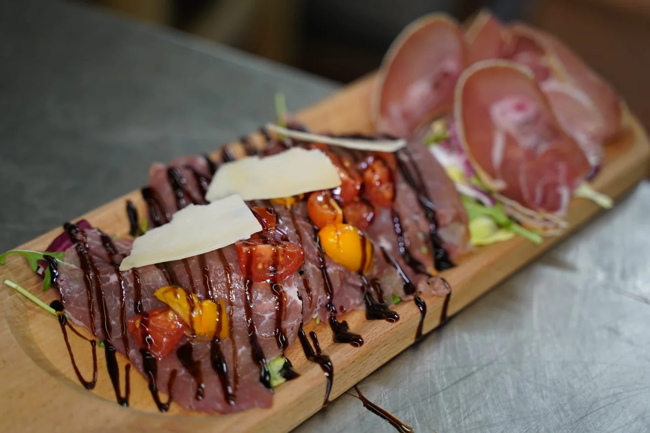 A board of beef carpaccio with cheese shavings, tomatoes and ham
