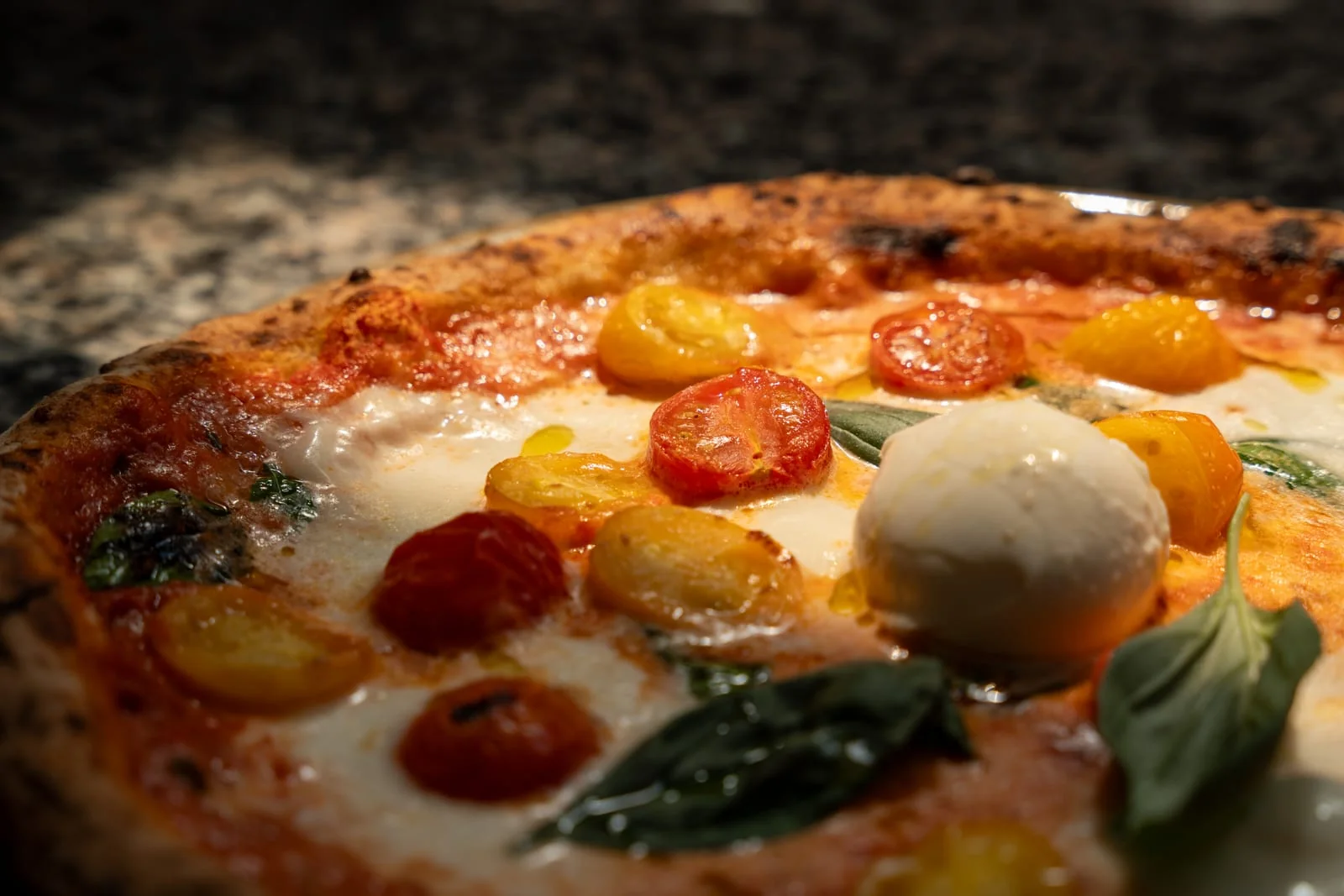 Una pizza appena sfornata con pomodorini gialli e rossi, mozzarella e basilico