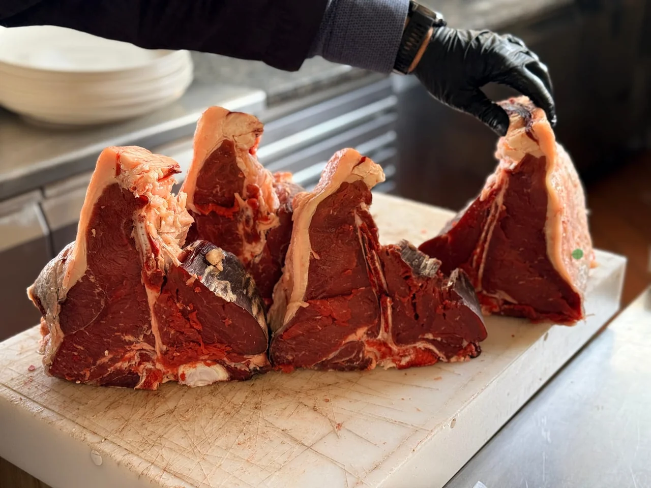 Four raw T-bone steaks on a chopping board, cut thick