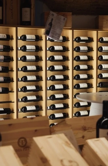 Le rastrelliere a muro della cantina, piene di bottiglie coricate, con le casse di legno in primo piano