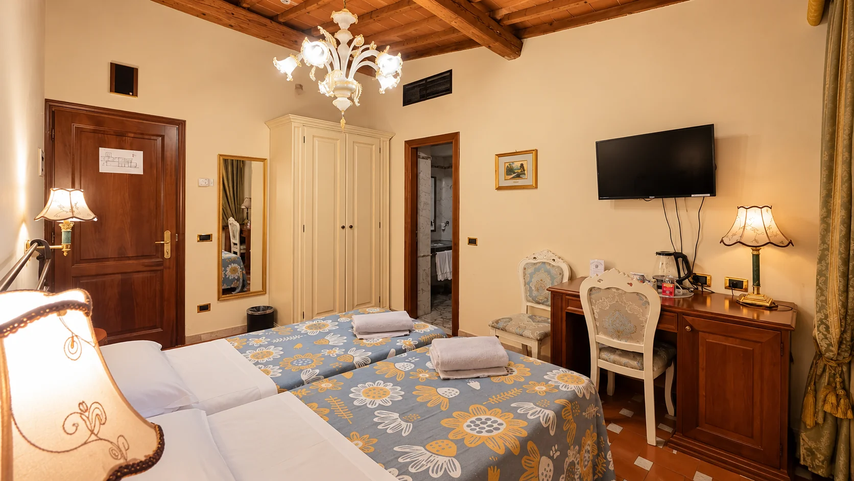 The Classic room seen from the beds, with a writing desk, television, wardrobe and bathroom entrance