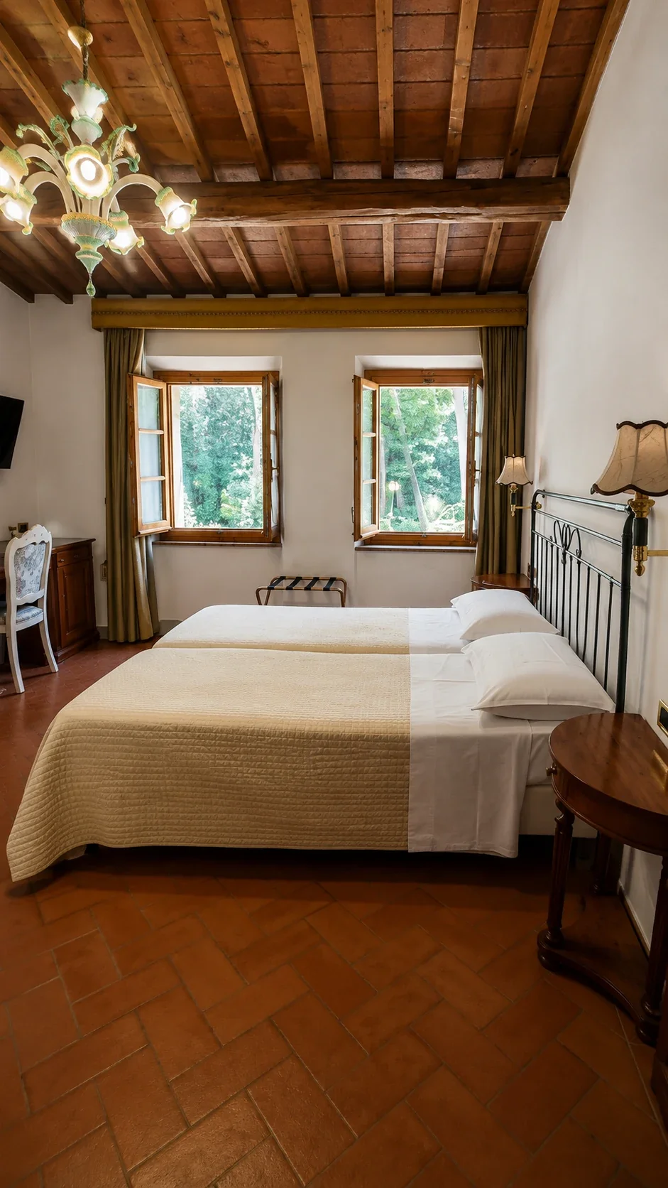 Il letto della Camera 409 sotto le travi a vista e davanti a due finestre incorniciate da tende chiare