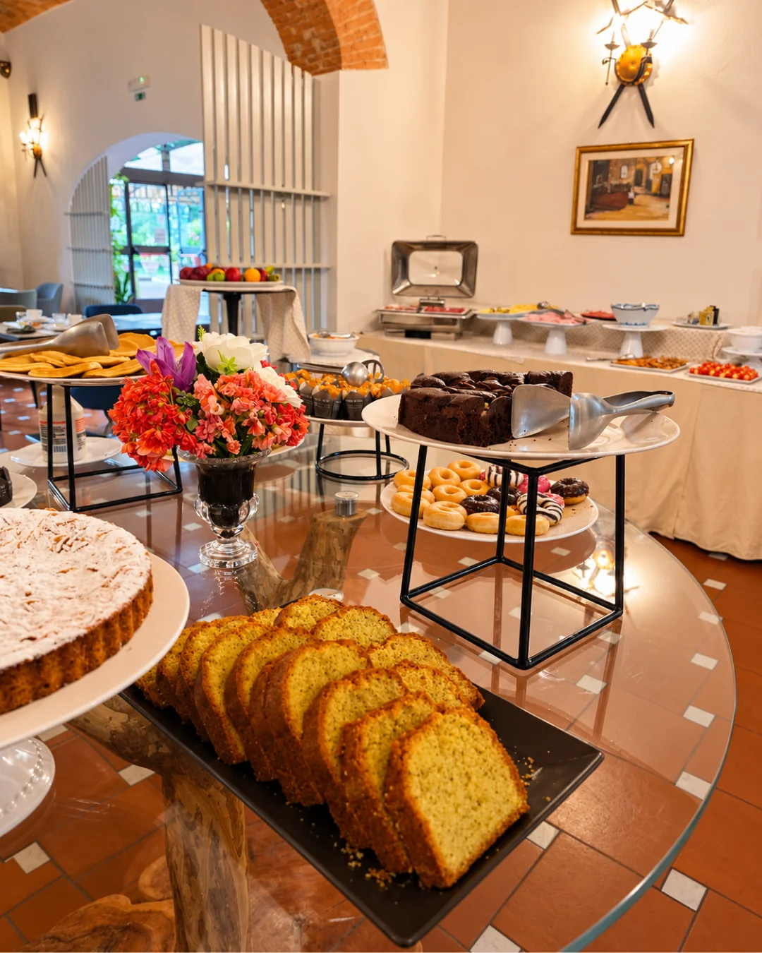 La sala della colazione sotto la volta in mattoni: il tavolo dei dolci in primo piano e il buffet salato lungo la parete