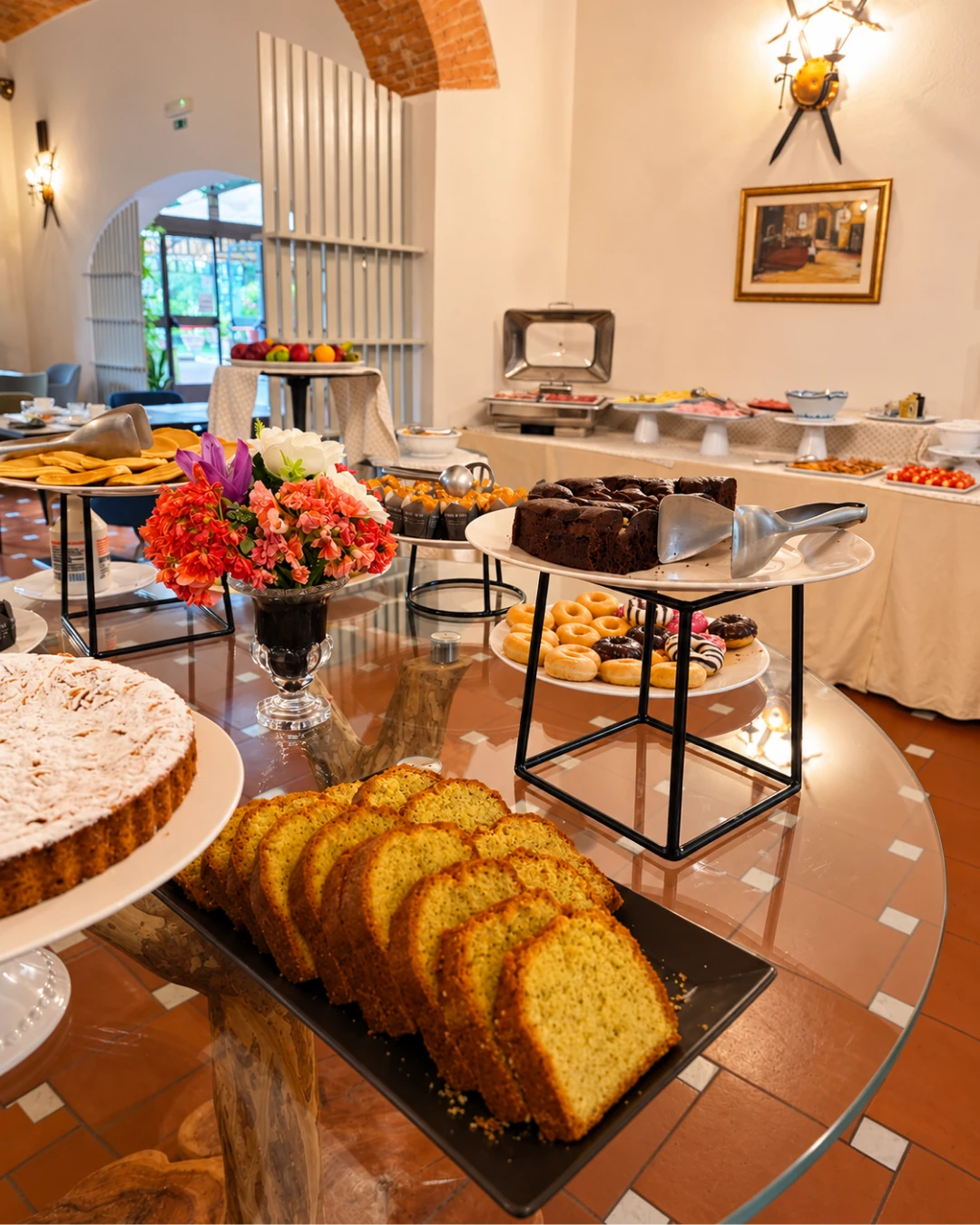 La sala della colazione sotto la volta in mattoni: il tavolo dei dolci in primo piano e il buffet salato lungo la parete