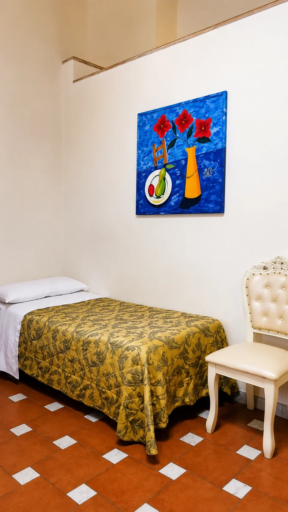 Il letto con copriletto damascato accanto a una sedia chiara e a un dipinto dai colori vivaci