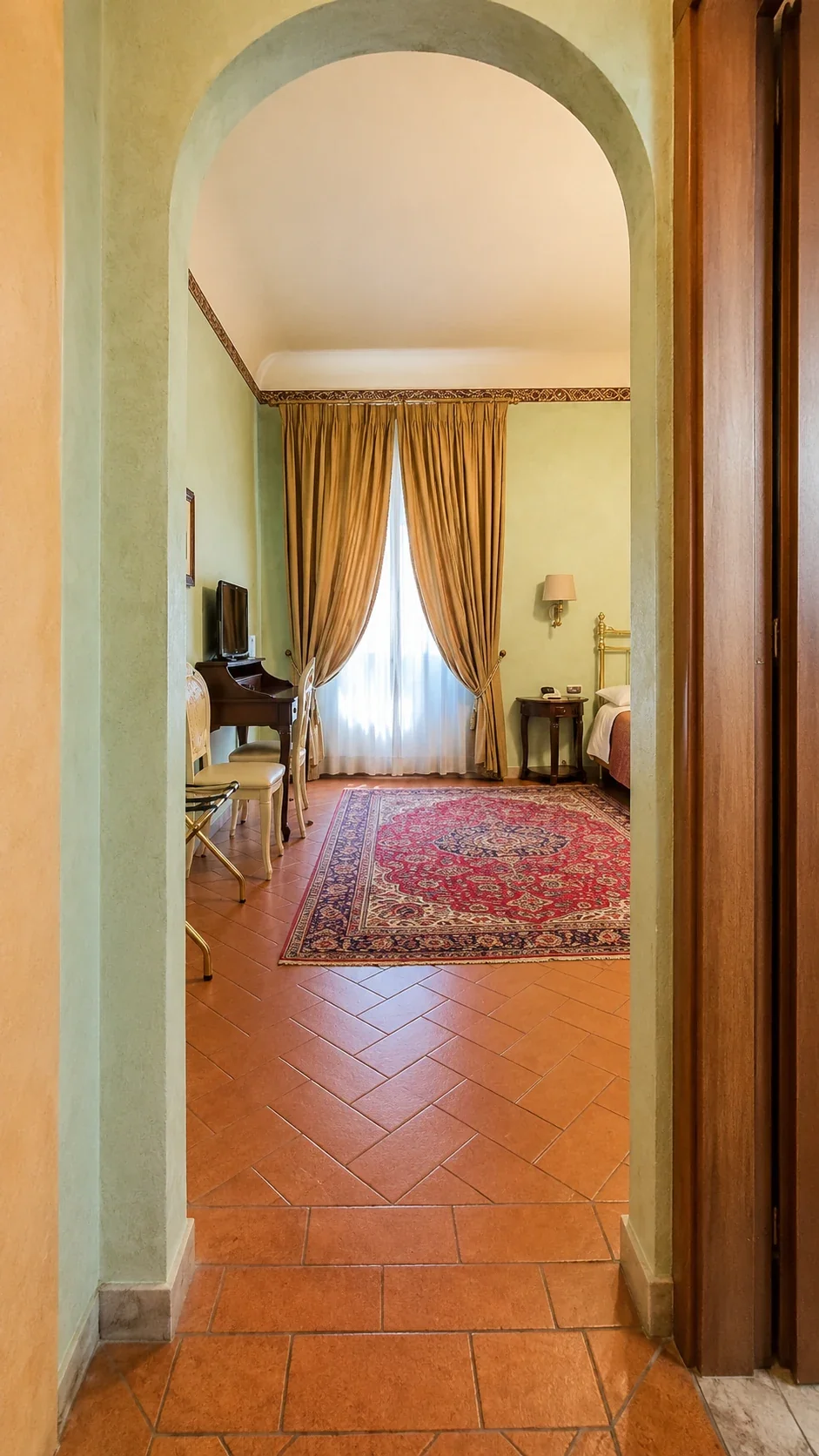L'ingresso ad arco della Camera 210 apre sul tappeto, sul letto e sulla finestra incorniciata dai tendaggi