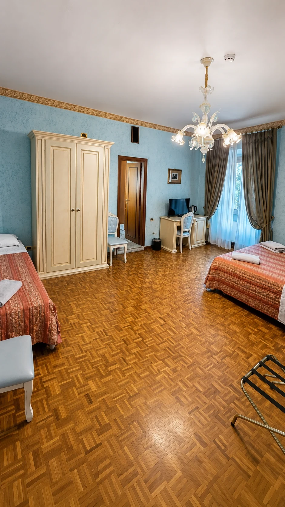 La Camera 212 con pareti celesti, pavimento in parquet e letti con copriletti color corallo