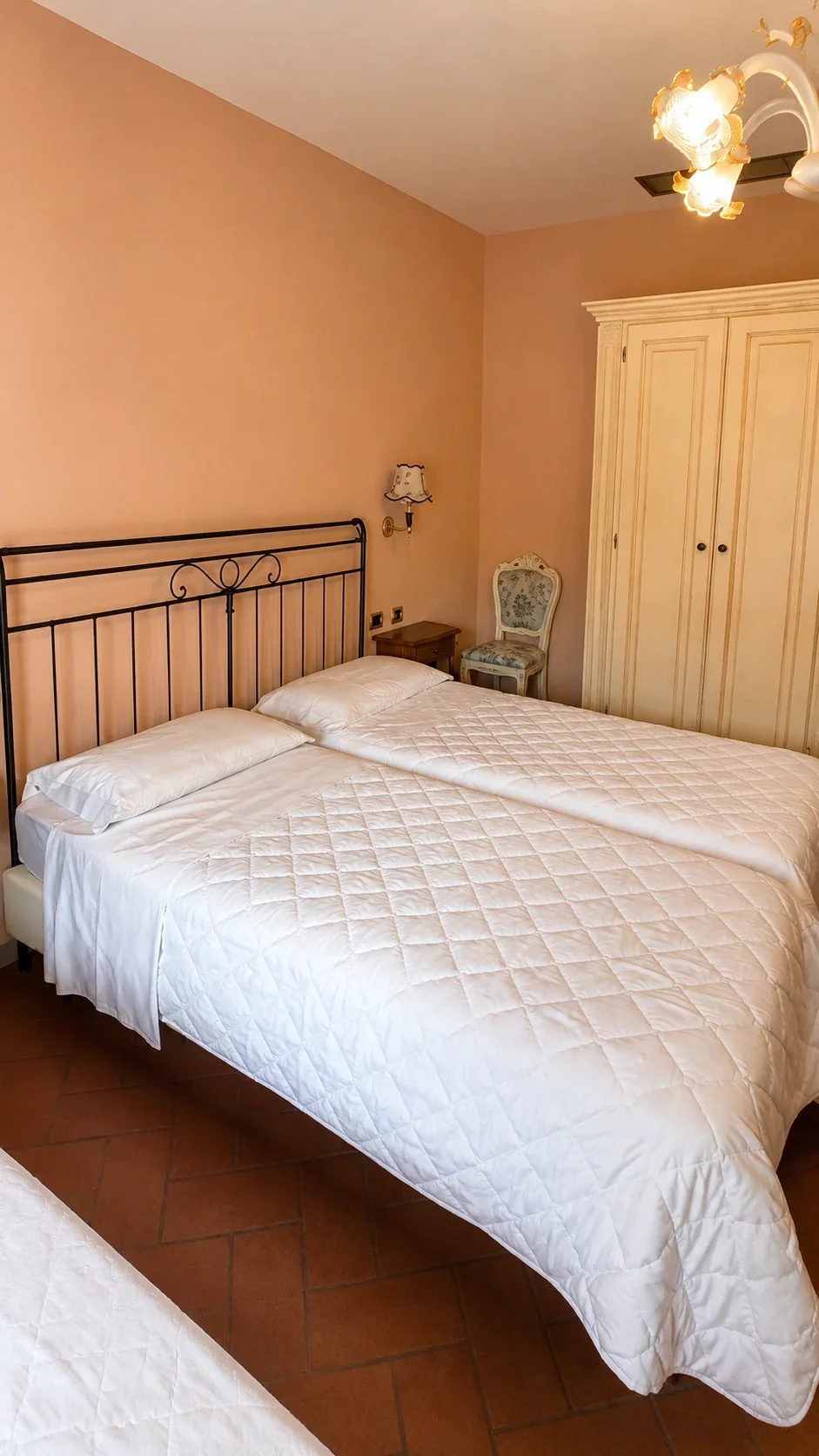 Il letto in ferro battuto e l'armadio chiaro contro la parete rosa della Camera 403