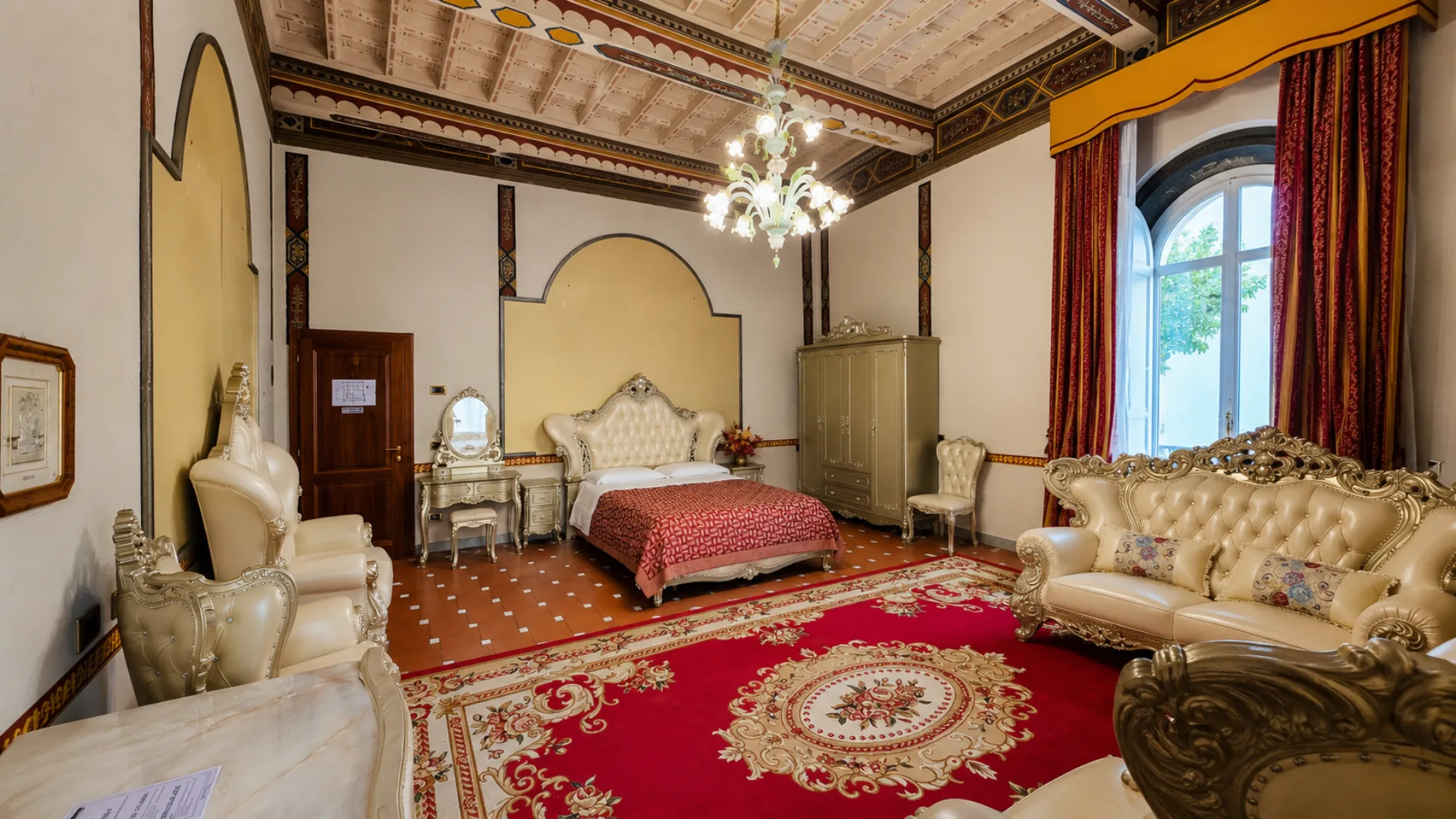 A Junior Suite of the villa: painted beamed ceiling, glass chandelier, tufted bed and the arched window with damask curtains