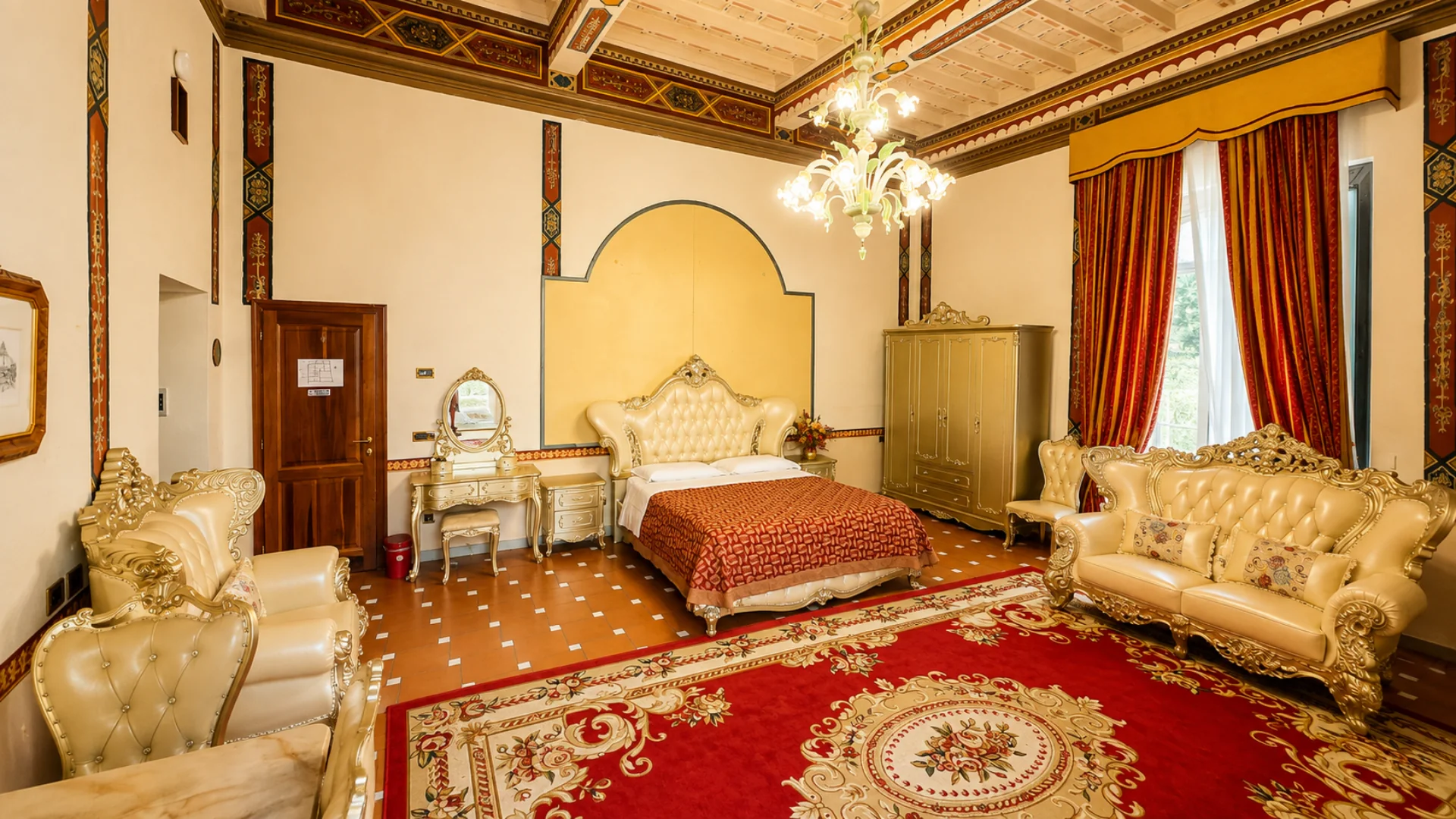 The tufted bed of the Junior Suite between the dressing table and the gilded wardrobe, with the red rug and damask curtains