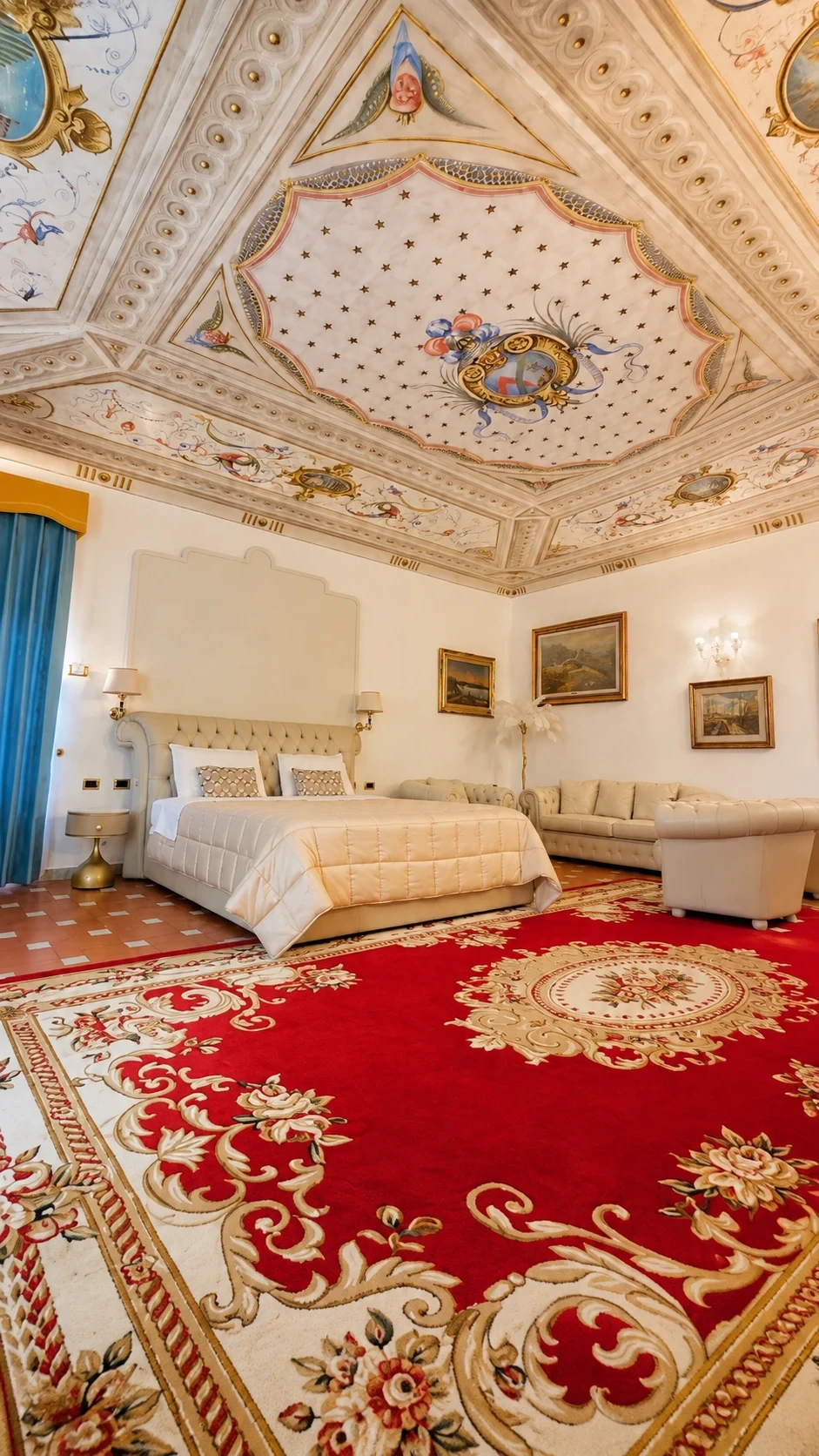 La Junior Suite 201 con letto, salotto, tappeto rosso e soffitto affrescato con lo stemma degli Ambrogi