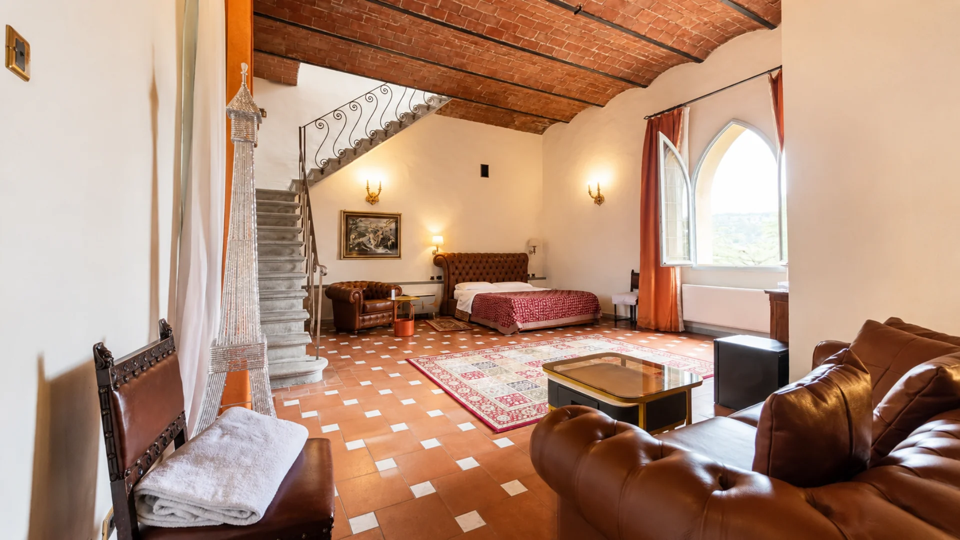 King deluxe 218 seen from the door: brick vault, stone stair to the mezzanine, tufted bed and a gothic arched window