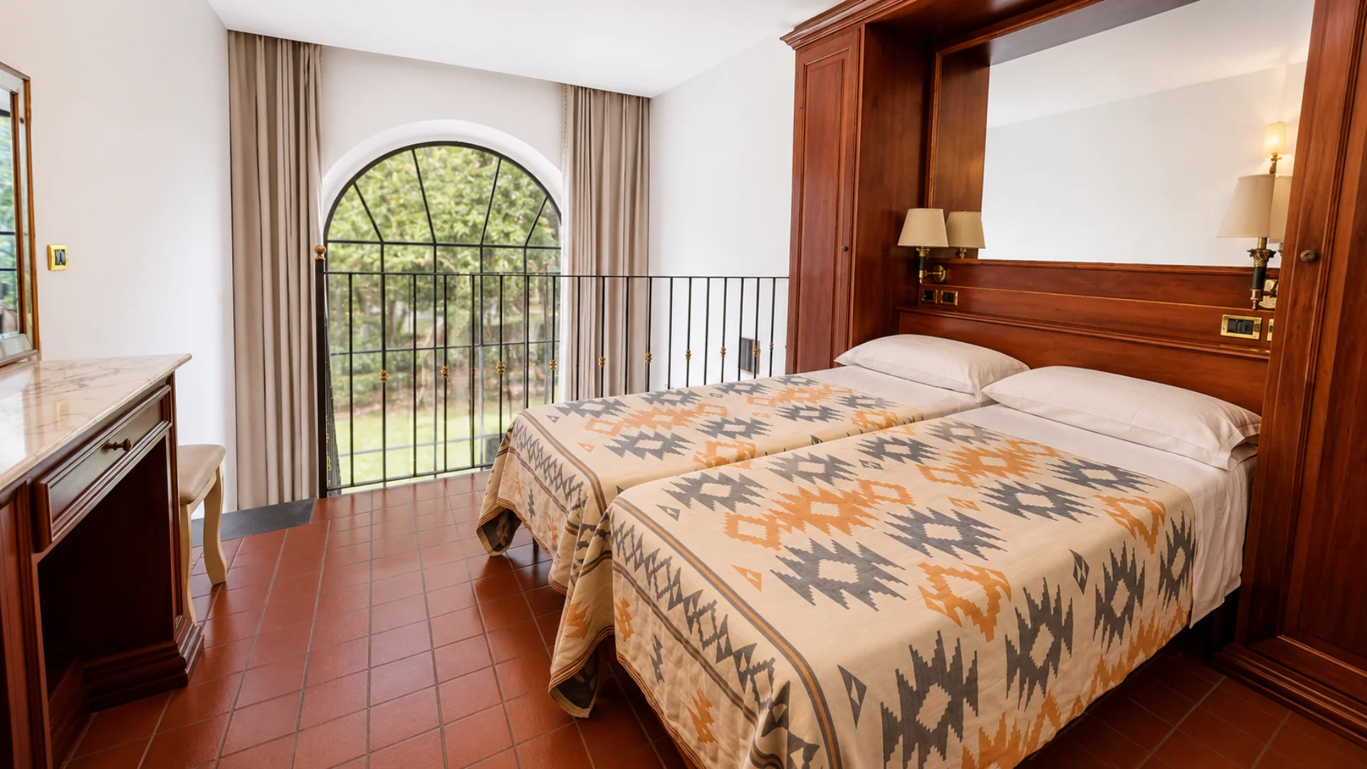 A loft with twin beds, a wooden headboard and an arched French window with a small balcony over the garden