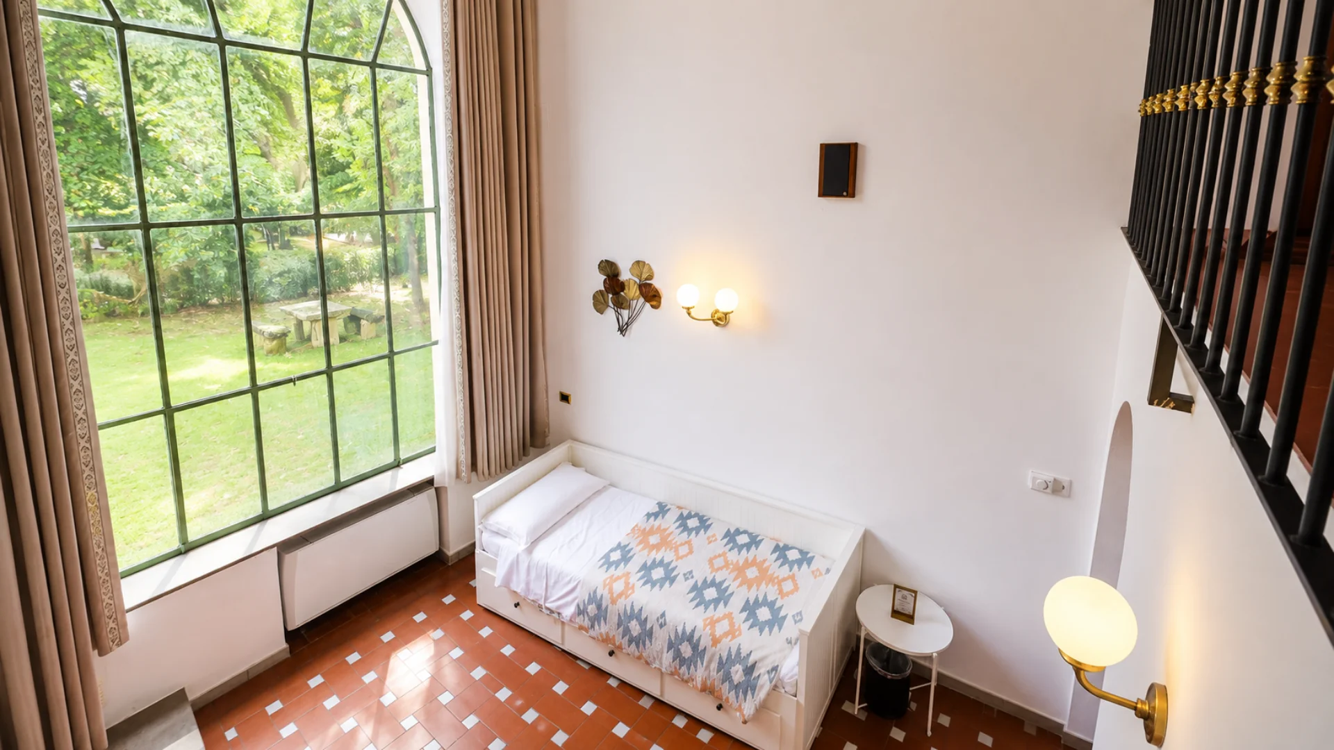 The day bed of a loft under the tall window onto the park, with the mezzanine railing on the right