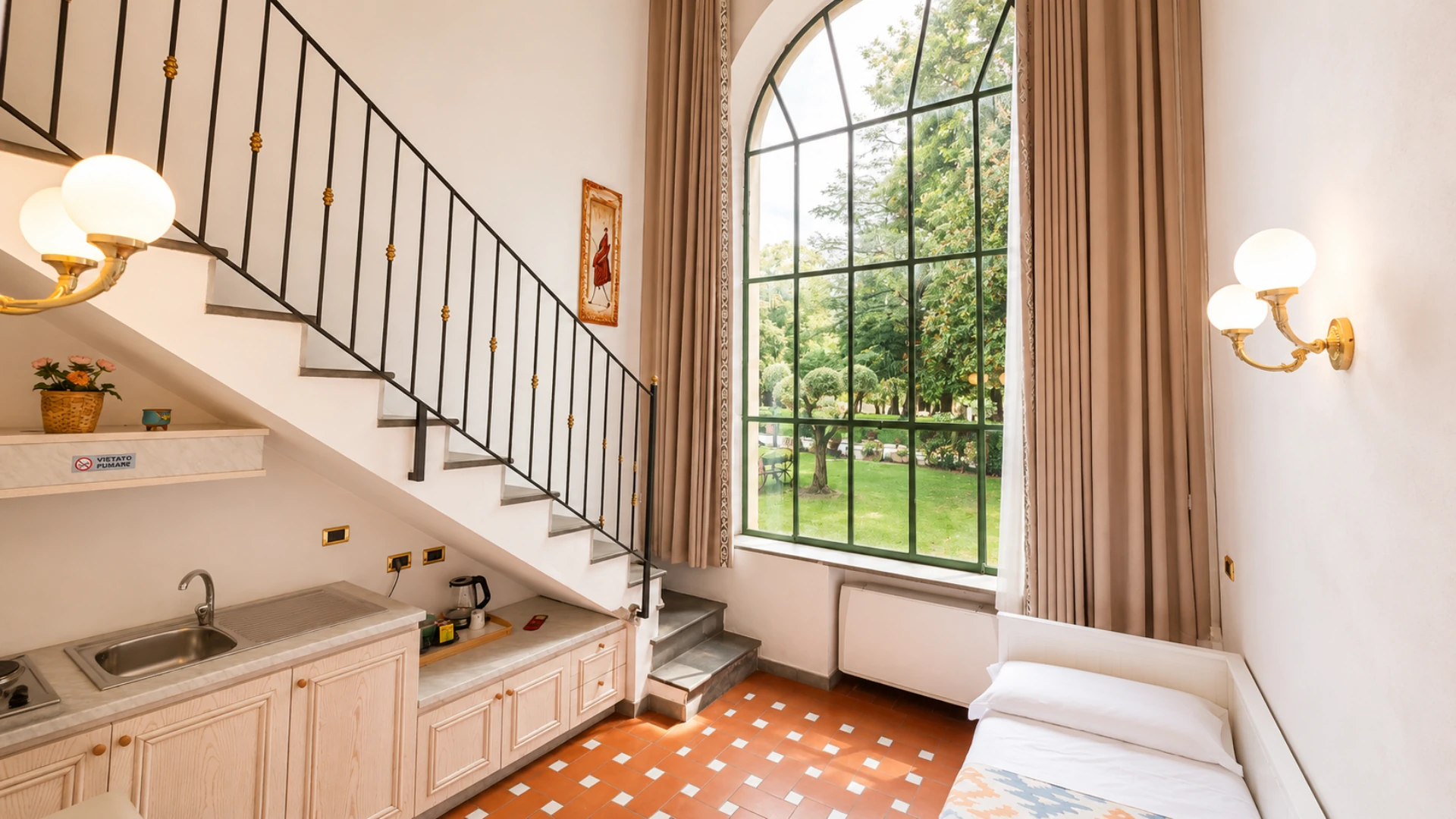 The entrance of a two-floor loft: the stair up to the mezzanine, the kitchenette and the tall window onto the park