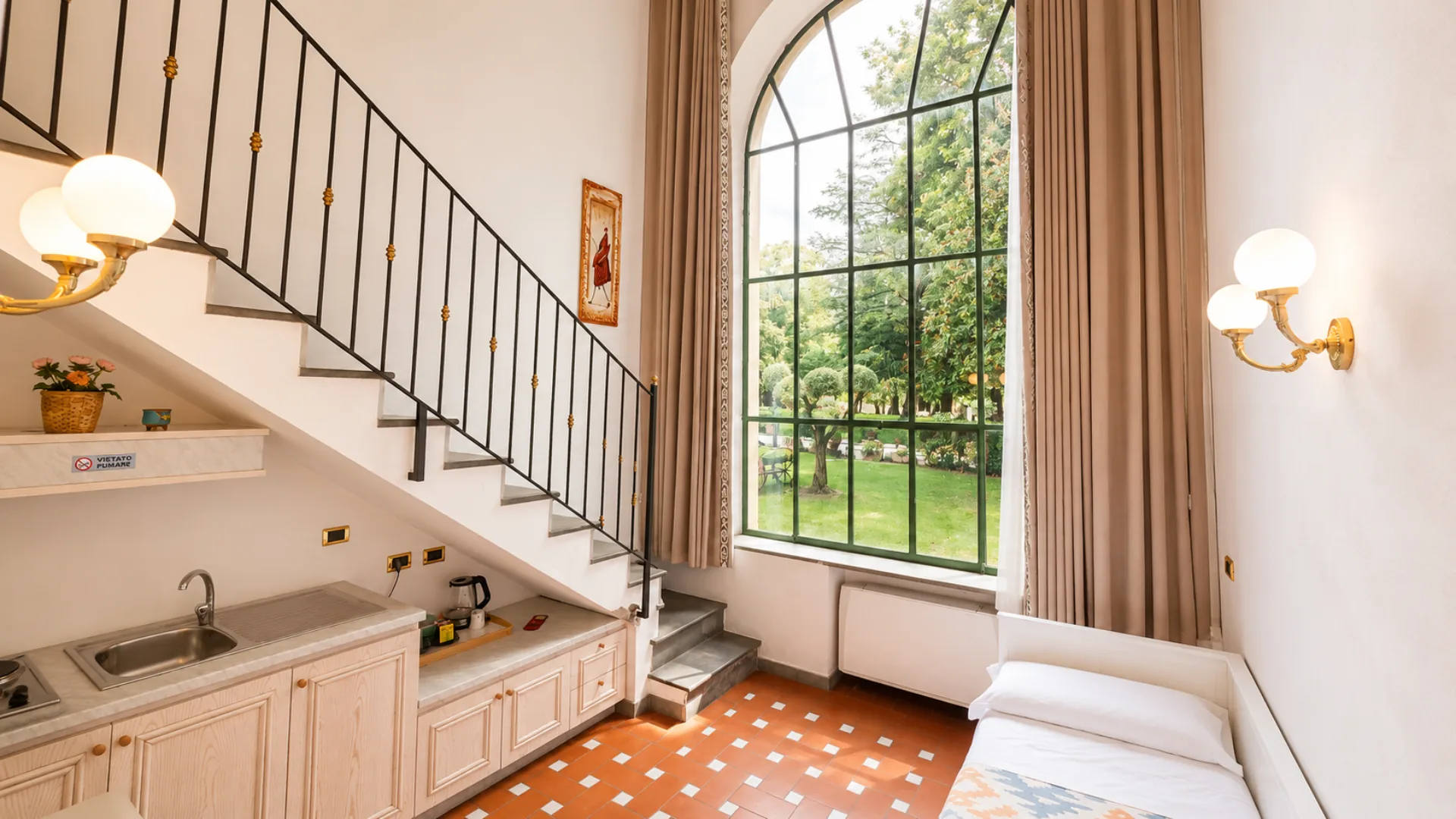 Un loft su due piani: la scala che sale al soppalco, l'angolo cottura e la vetrata alta sul parco