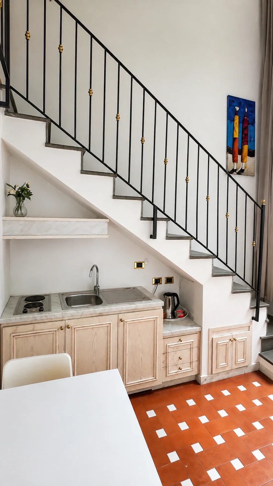 La cucina compatta del Loft 302 inserita sotto la scala con ringhiera nera e dettagli dorati