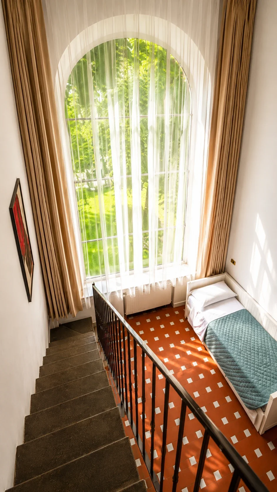 Il letto singolo del Loft 305 accanto alla finestra schermata da tende chiare sul giardino