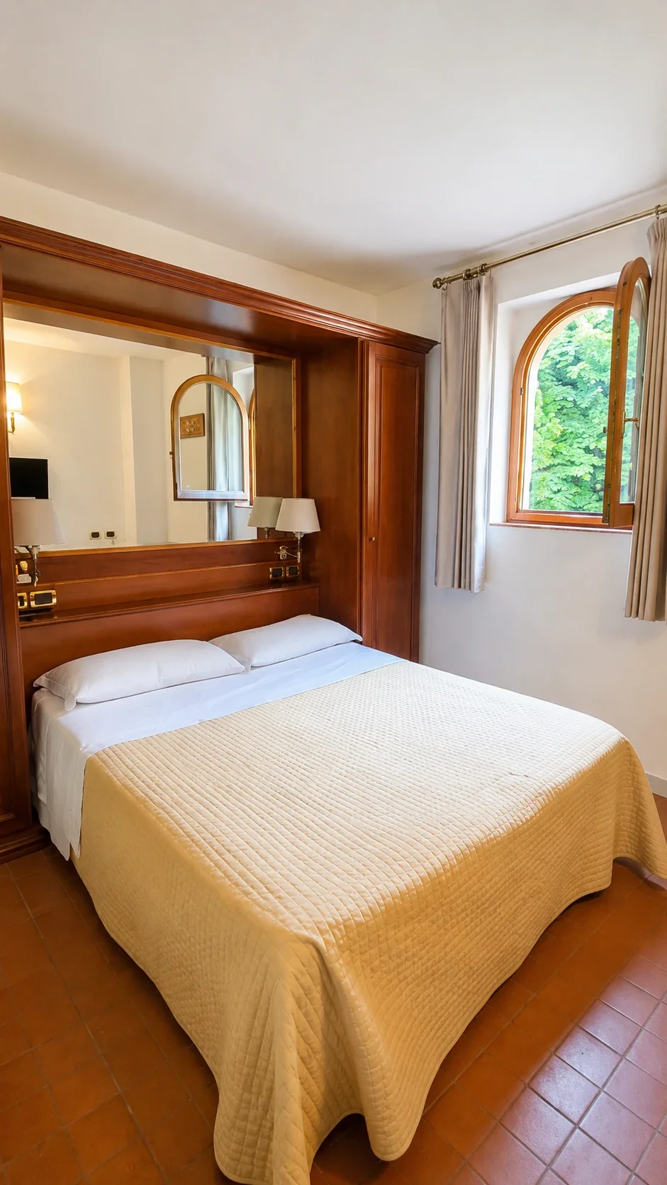 Il letto del Loft 306 con testata in legno, specchio e finestra laterale sulla vegetazione