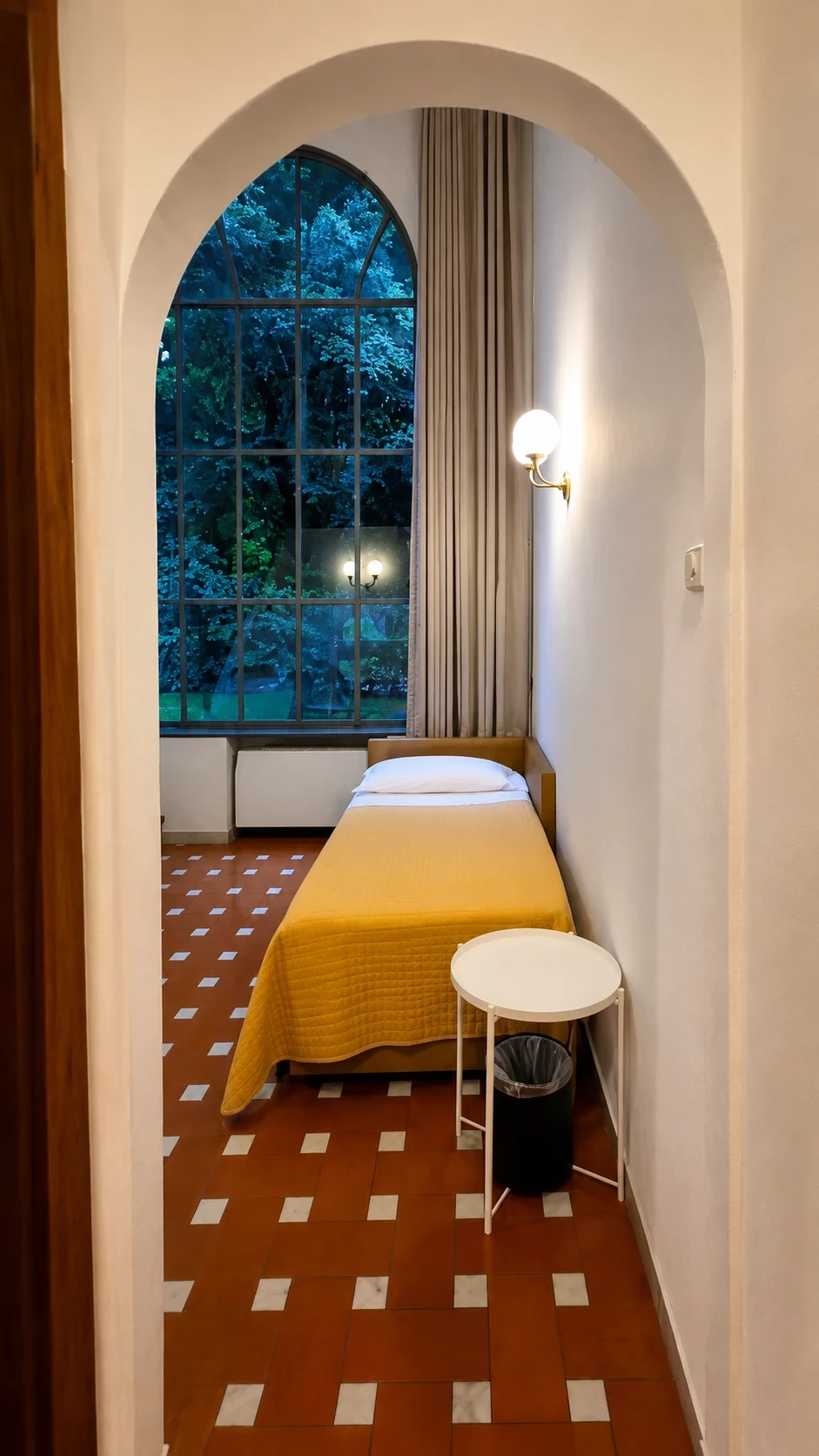 Il letto singolo al piano inferiore del Loft 308 davanti alla finestra sul giardino al crepuscolo