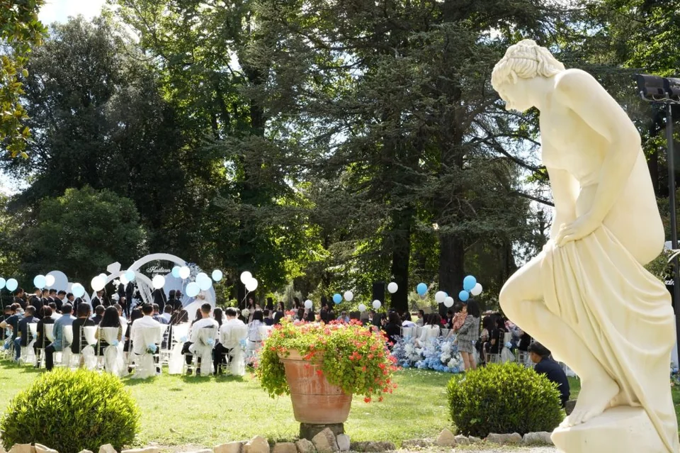 Una cerimonia nel parco della villa, con gli ospiti seduti fra gli alberi e i palloncini bianchi e azzurri