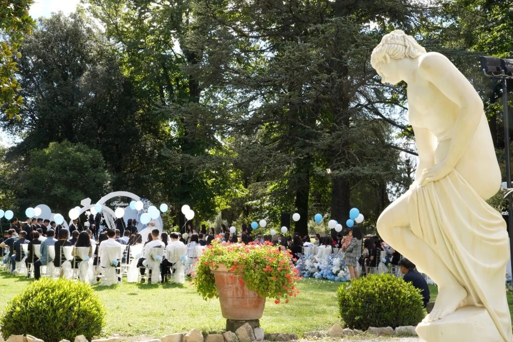 Una cerimonia nel parco della villa, con gli ospiti seduti fra gli alberi e i palloncini bianchi e azzurri