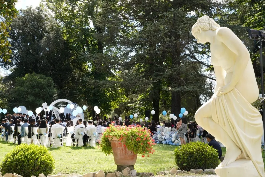 Una cerimonia nel parco della villa, con gli ospiti seduti fra gli alberi e i palloncini bianchi e azzurri