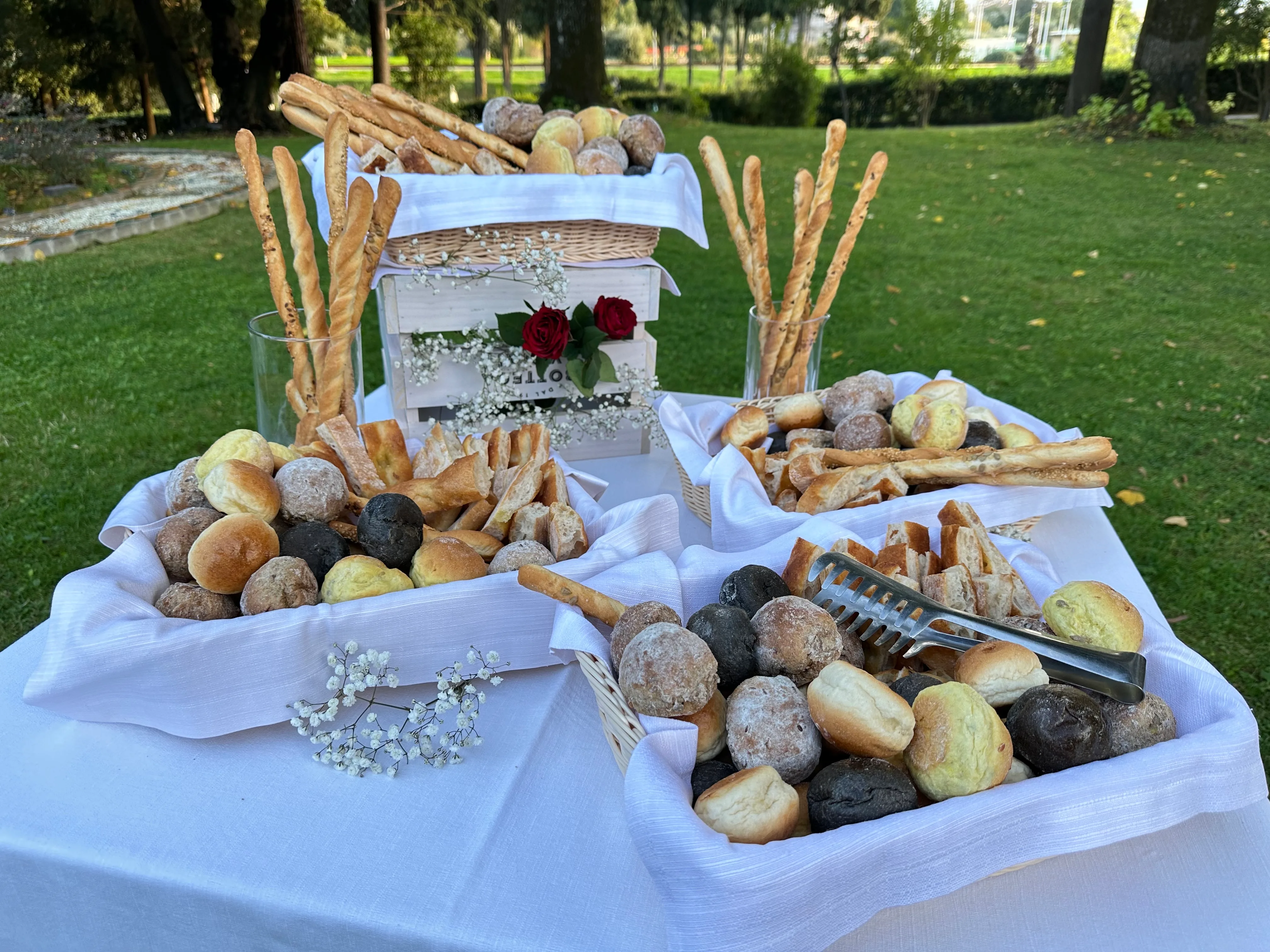 The brunch buffet laid out in the park: baskets of bread, grissini and brioches on a white cloth