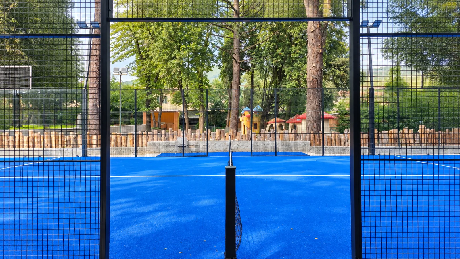 La rete al centro del campo vista da dietro la vetrata, con gli alberi del parco e i giochi dei bambini sullo sfondo