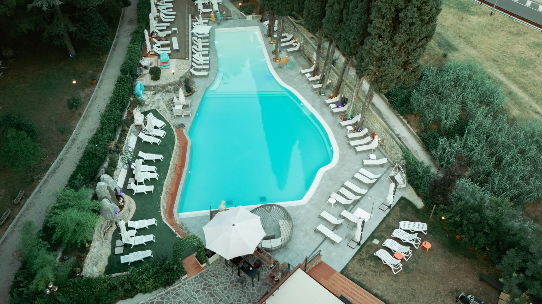 The pool from above at dusk, loungers all around and the lights on