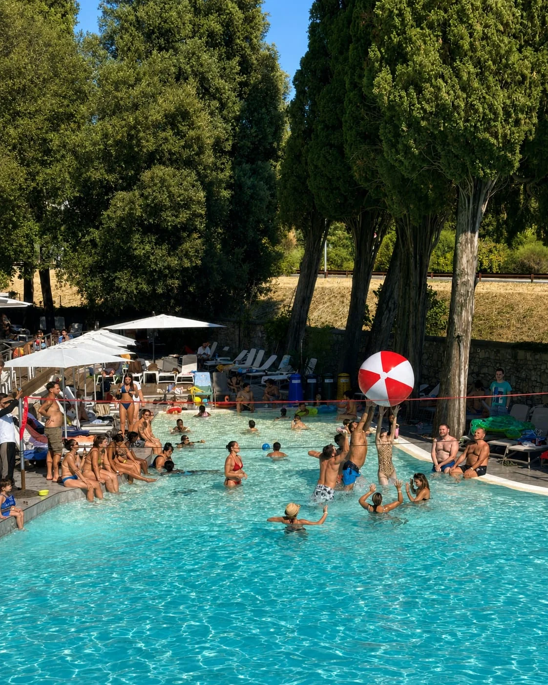 La vasca piena di gente che gioca con un pallone, in una giornata d'agosto