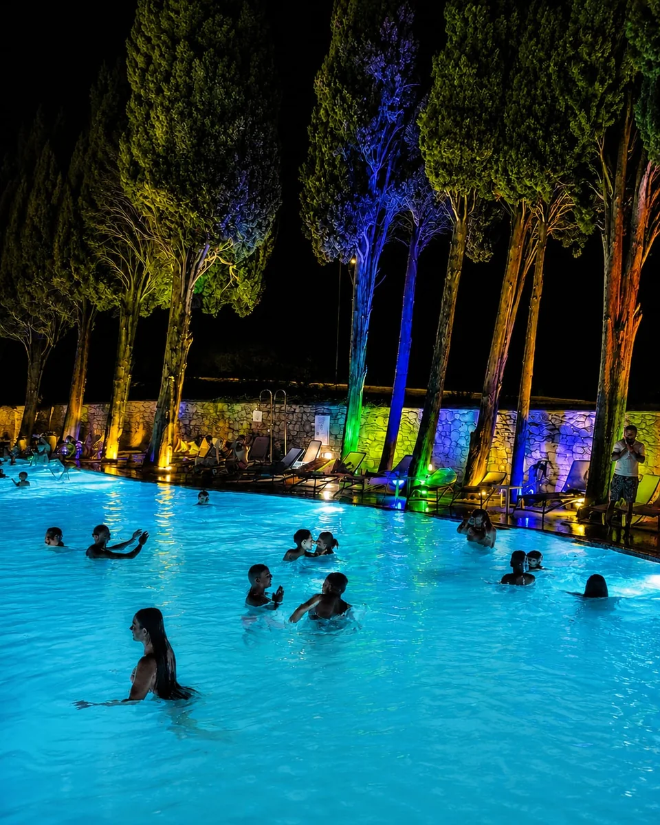 The pool at night, with the cypresses lit in blue, green and orange