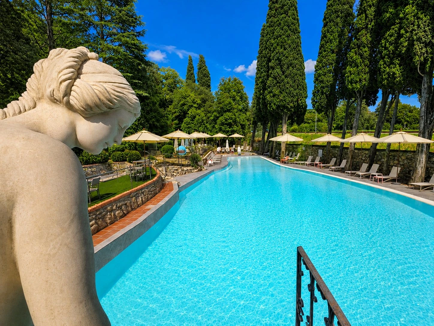The pool among the cypresses seen past the statue, umbrellas lined up
