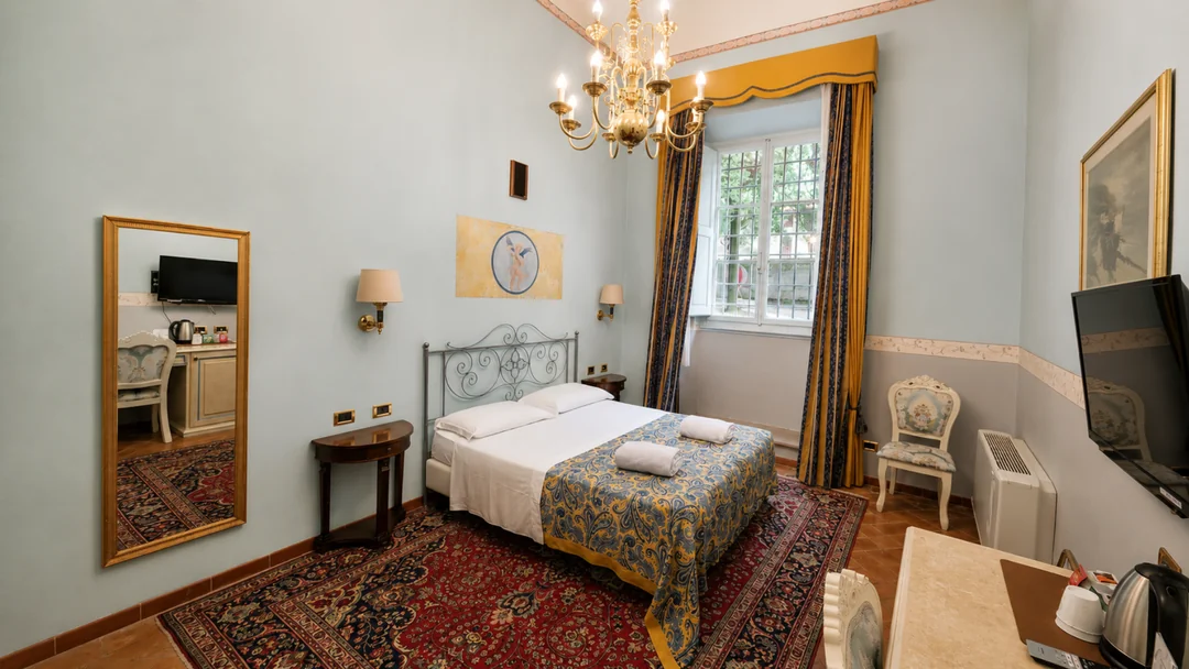 Una camera Premium azzurra con il letto in ferro battuto, il lampadario a bracci e le tende gialle e blu