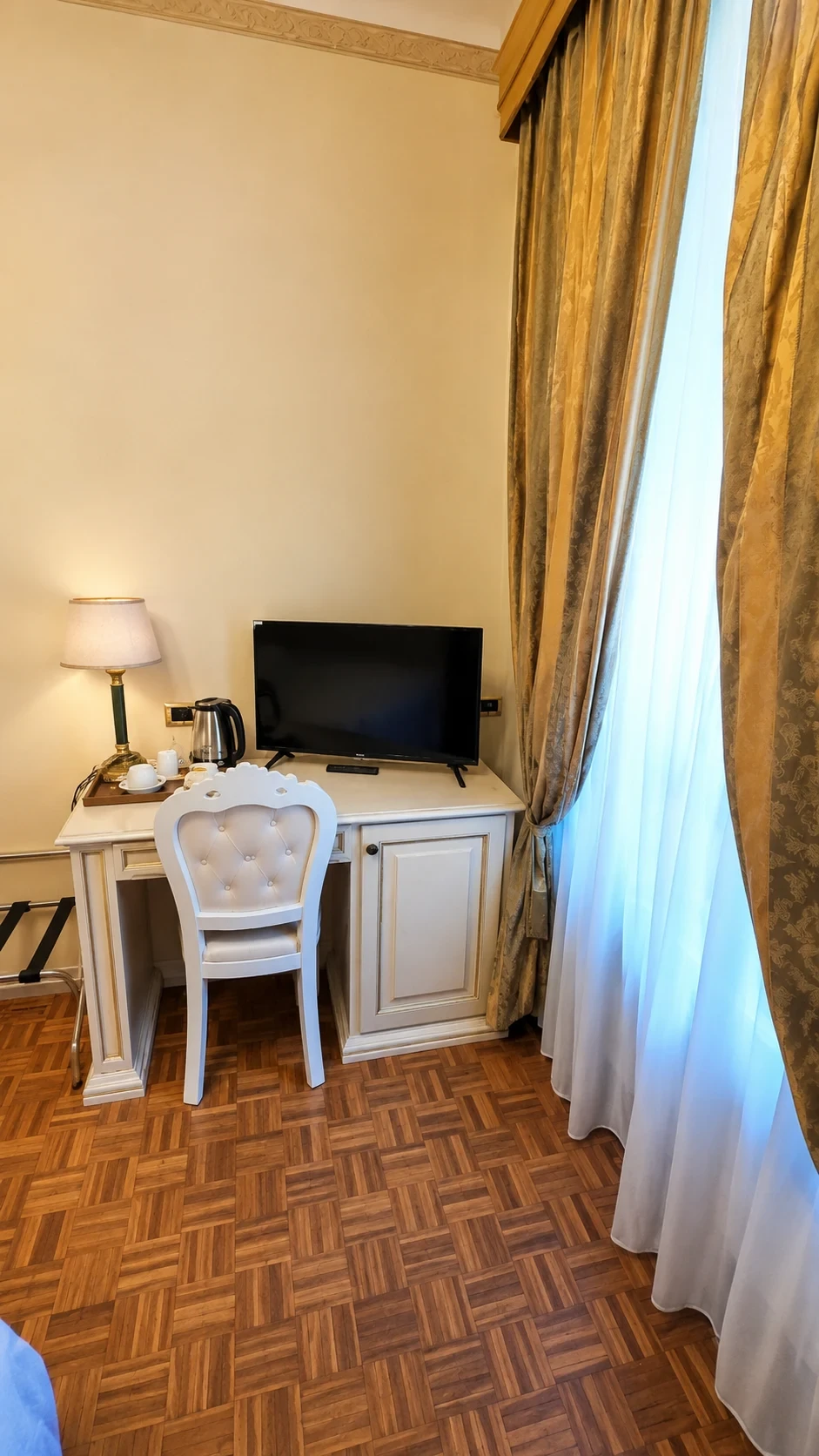 Lo scrittoio chiaro, il televisore e la finestra con tende dorate nella Camera Vegoia