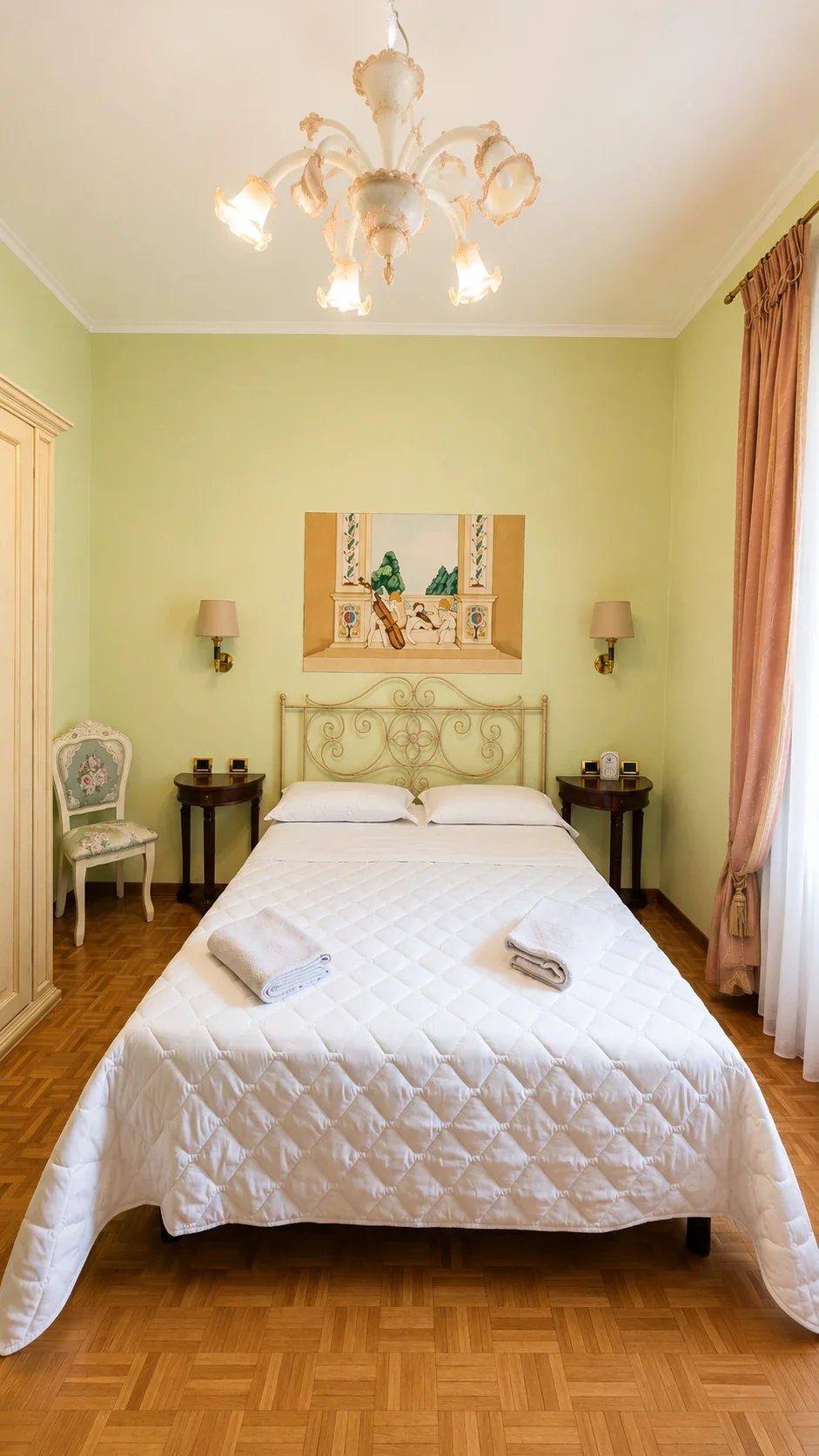 Il letto della Camera Terpsicore tra le pareti verde chiaro e il lampadario in vetro