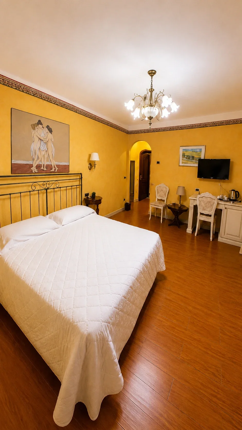 La Camera 214 dedicata alle Tre Grazie La Camera 214 dalle pareti ocra con letto matrimoniale, dipinto delle Tre Grazie e scrittoio chiaro