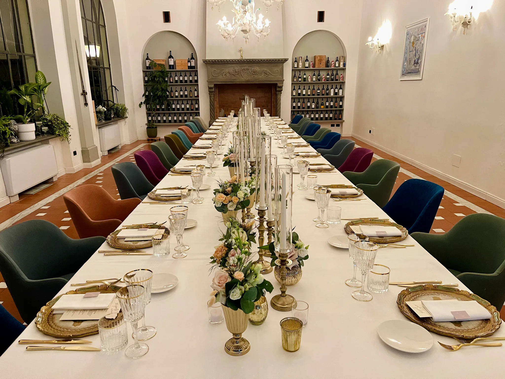 The restaurant hall set for a banquet: the long table with candelabra and flowers, coloured velvet chairs, the fireplace and the wine shelves