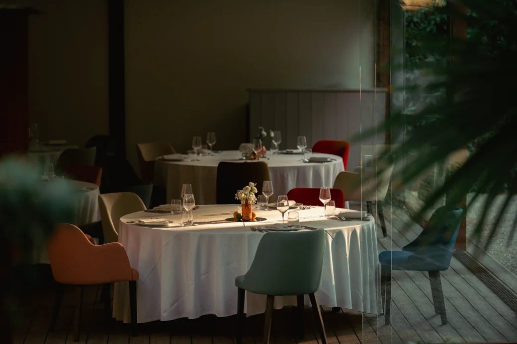 Round tables laid in the evening, with warm light coming through the glass wall onto the park