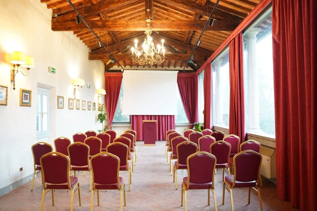 La sala meeting con le sedie in fila, le tende rosse e le travi a vista