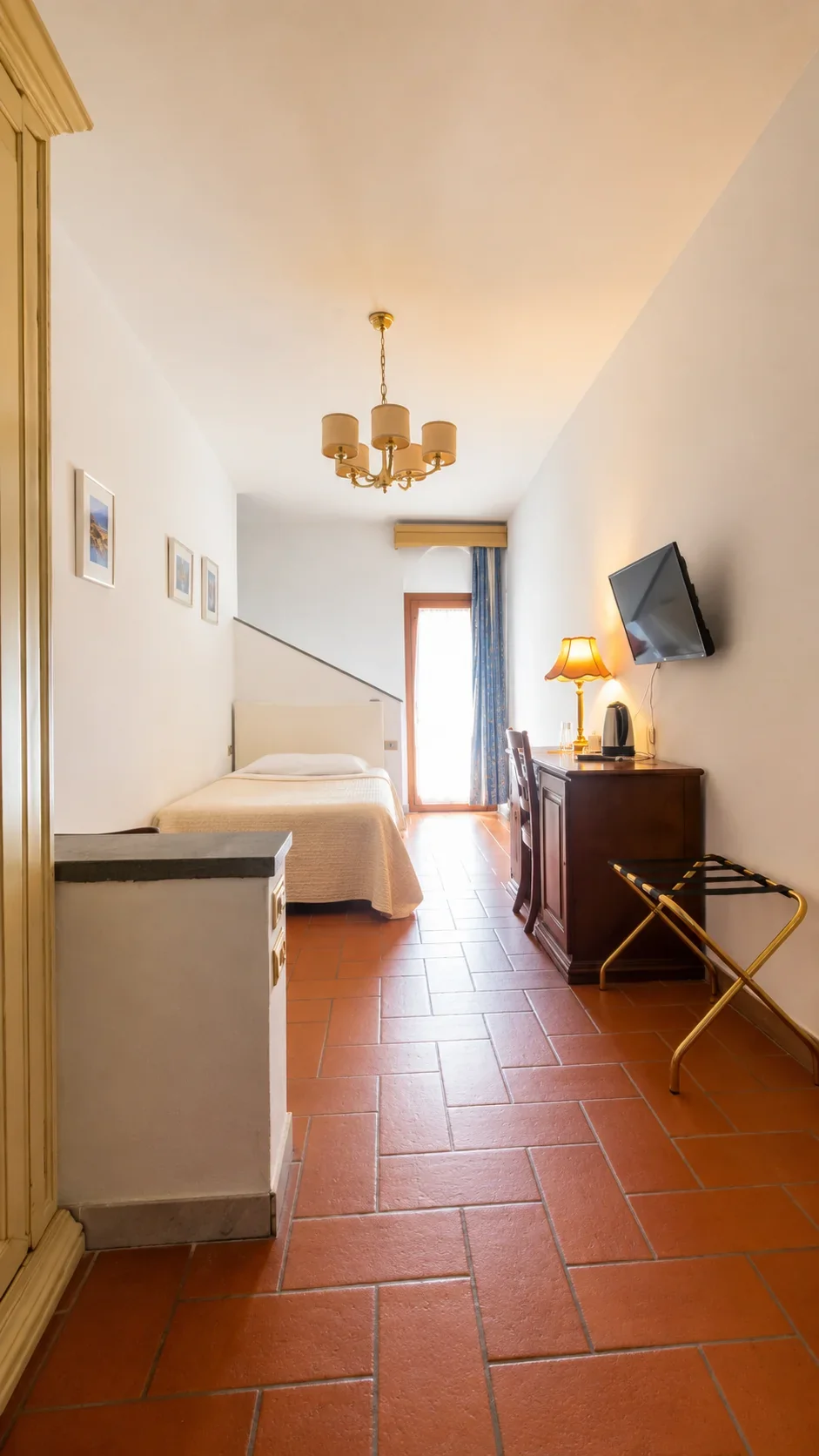 La Camera 404 vista dall'ingresso con letto, scrittoio, televisore e portafinestra affacciata sulla Limonaia