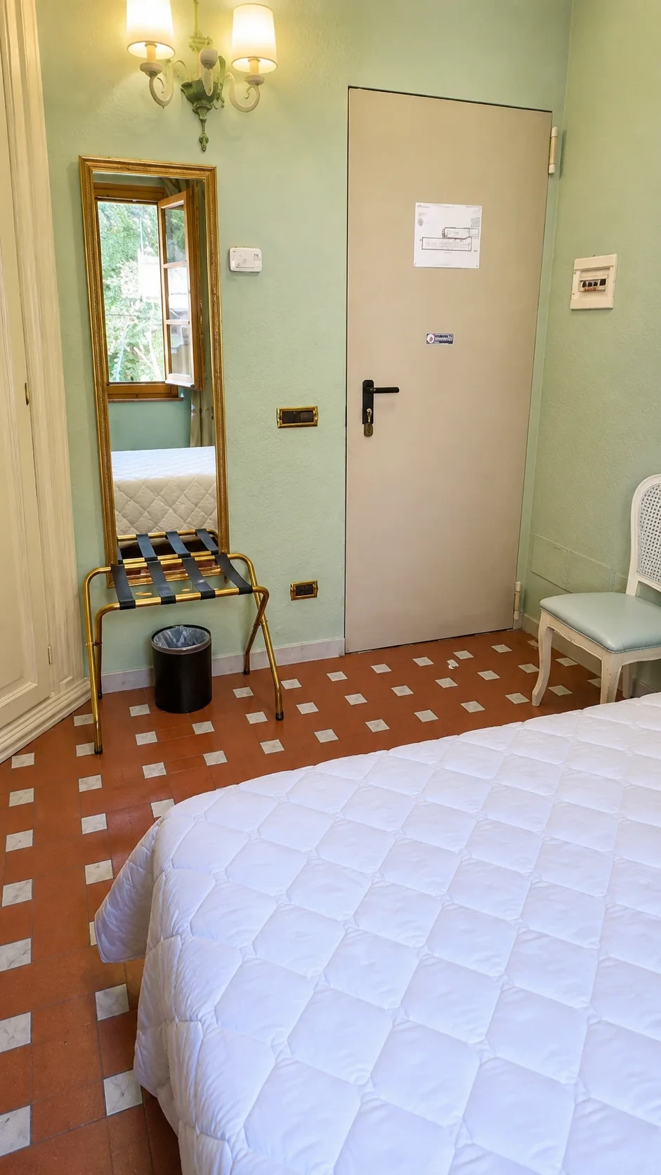 L'ingresso della Camera Egeria con specchio dorato, portavaligie, armadio chiaro e pavimento in cotto decorato