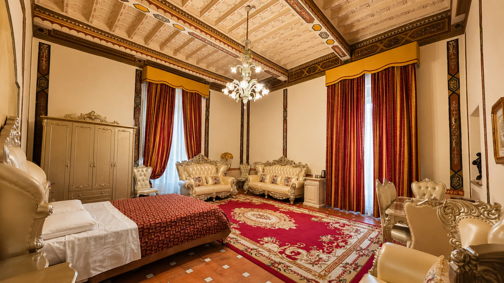 Una camera della villa: il soffitto a cassettoni dipinto, il lampadario in vetro, le tende rosse e il tappeto sul pavimento in cotto