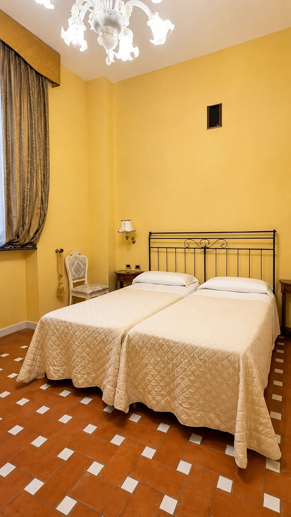I due letti singoli della Camera Hypate sotto la testiera in ferro battuto, tra comodini in legno e pareti color ocra