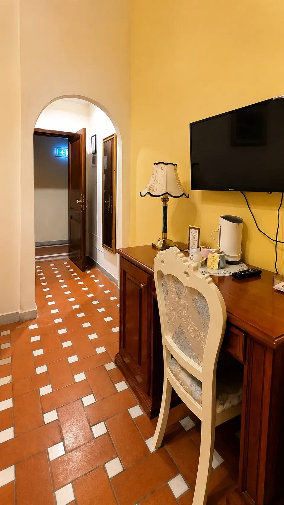 Lo scrittoio in legno della Camera 314 con sedia imbottita, lampada classica, televisore e passaggio ad arco
