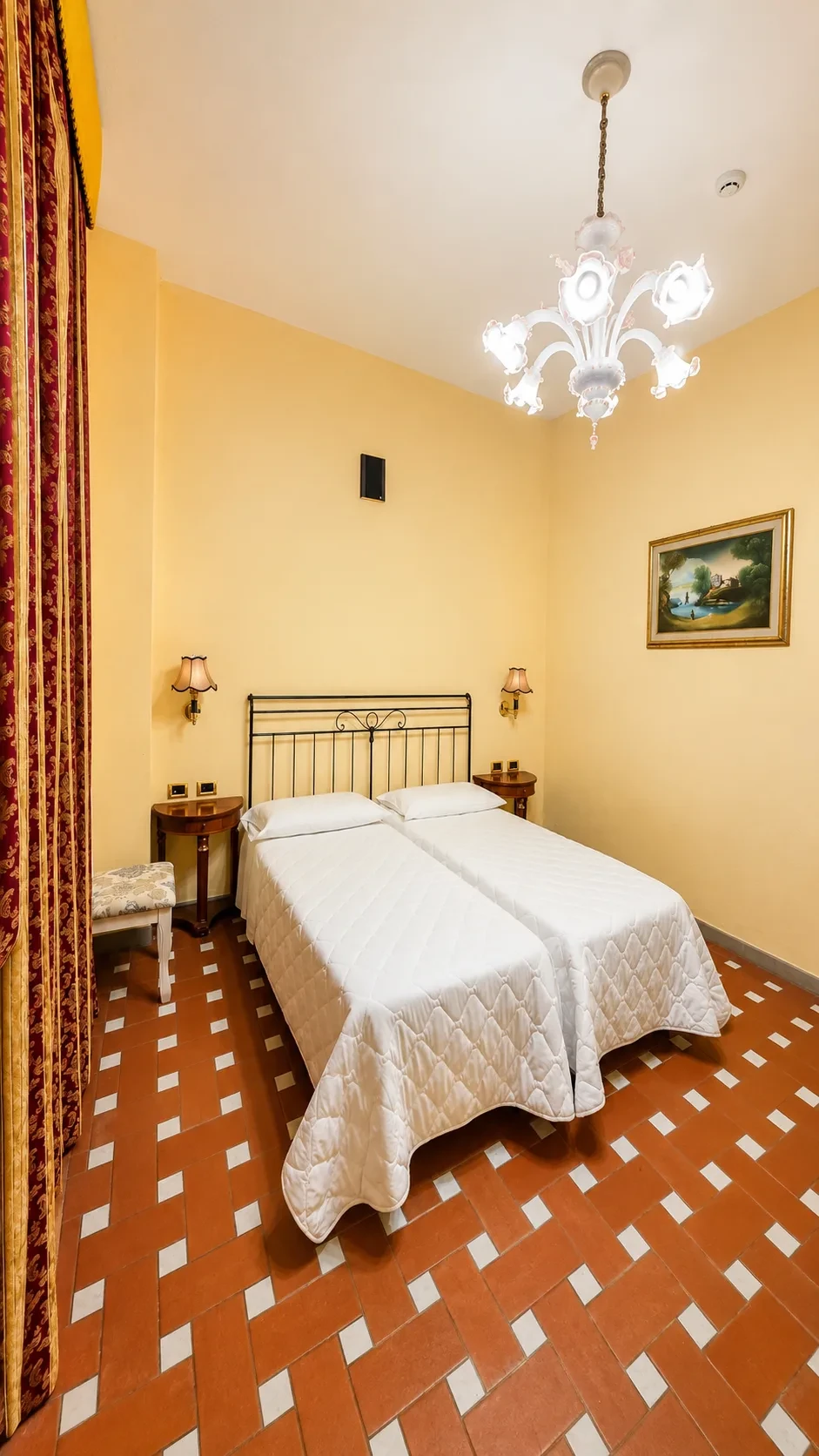I due letti singoli della Camera Fufluns fra comodini in legno, applique e tende rosse decorate in oro